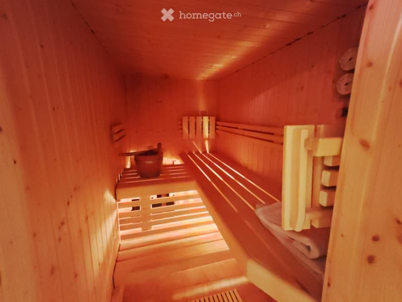 Wooden sauna with multiple benches and a wooden bucket on the left side.
