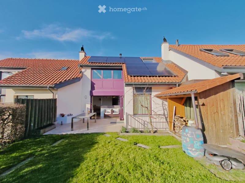Two-story house with red-tiled roof, solar panels, white and pink exterior, patio with outdoor furniture, and a well-maintained lawn.