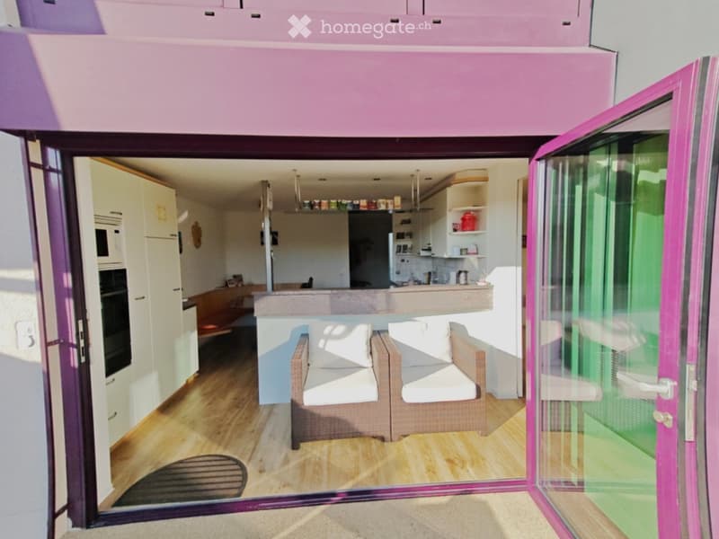 Open-plan living and kitchen area with a sofa, bar counter, and modern kitchen cabinets. Large glass doors lead to a balcony.