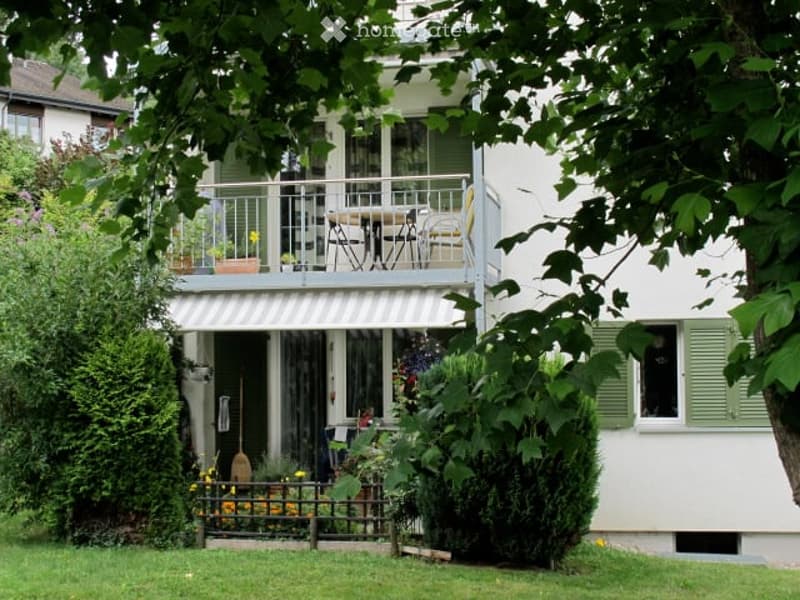 Two-story house with white exterior, green shutters, and a balcony with outdoor furniture.