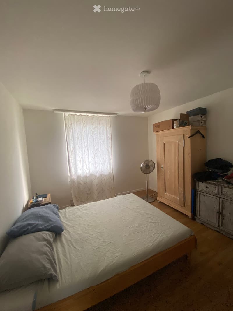 A small bedroom with a single bed, a nightstand, a fan, a cabinet, and a window with a curtain.