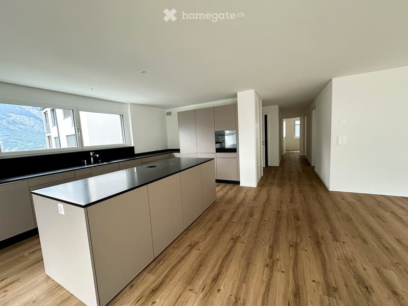 Modern kitchen with light-colored cabinets, black countertops, and a central island. Large windows offer a scenic mountain view.