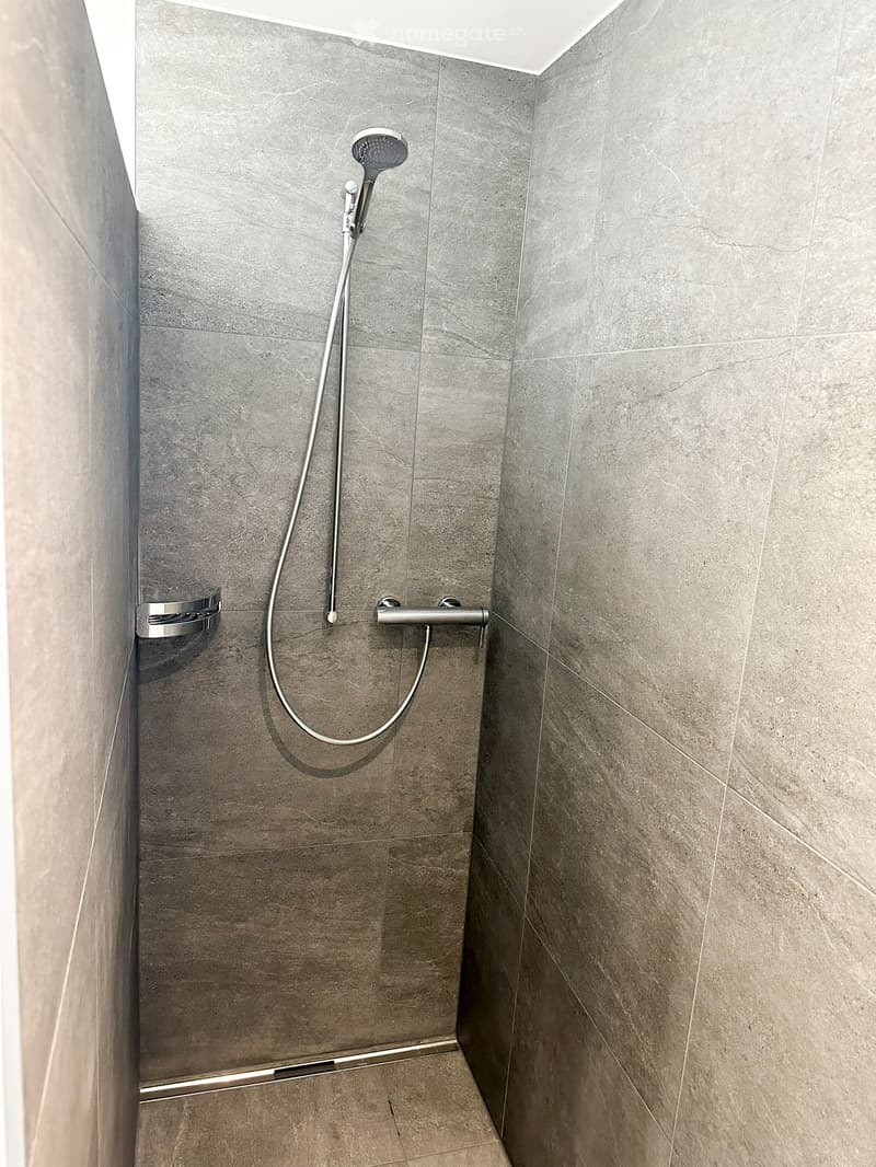 Modern shower area with grey marble tiles, a handheld showerhead, and a built-in shower rail.