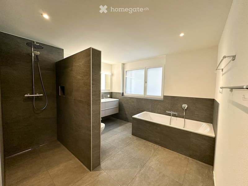 Modern bathroom with a bathtub, shower, sink, and toilet. Features large windows and built-in storage.