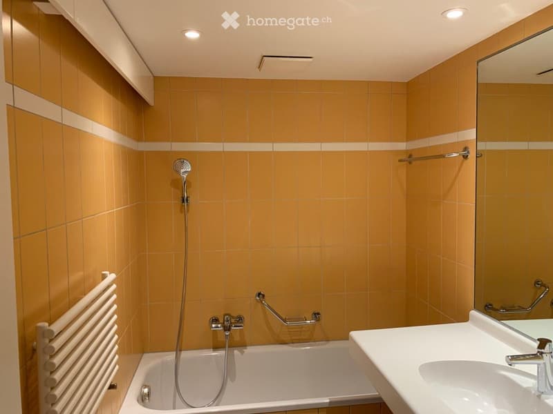 Modern bathroom with yellow tiles, a bathtub, a sink, a mirror, a showerhead, a radiator, and a towel rack.