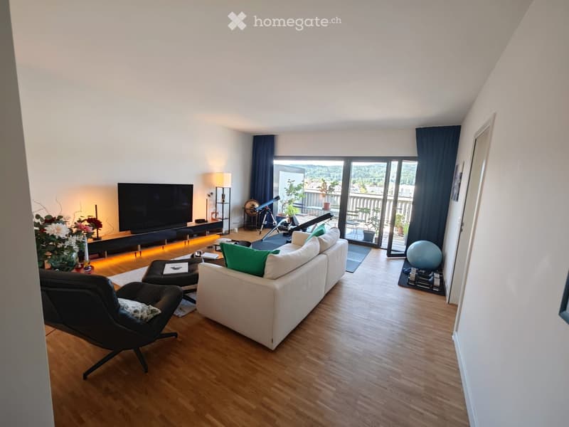 Modern living room with wooden flooring, large windows, balcony access, sofa, coffee table, TV, and decorative items.