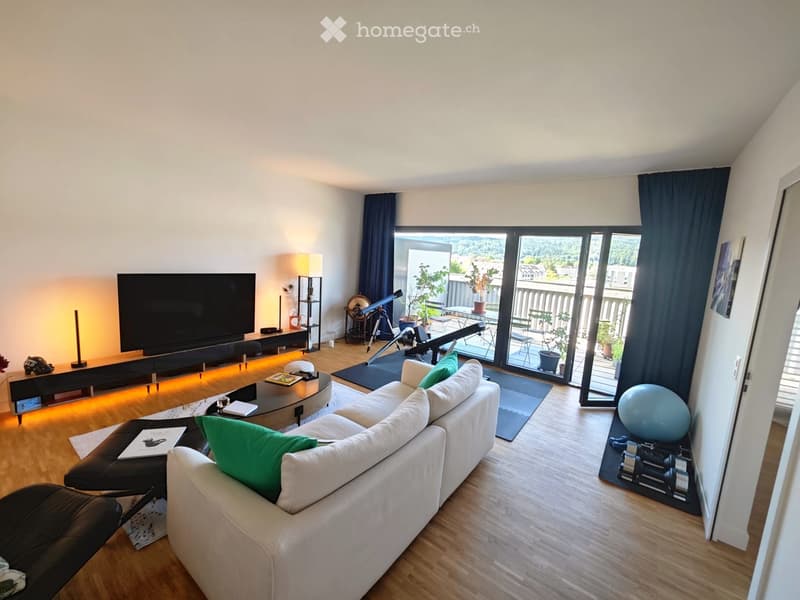 Modern living room with large windows and a balcony, featuring a white sectional sofa, coffee table, TV, and a telescope on the balcony.