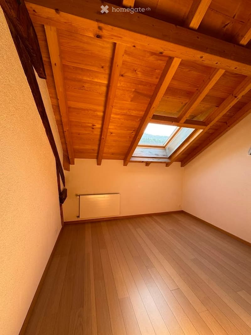 Empty room with wooden floor, exposed wooden ceiling beams, skylight window, and radiator.