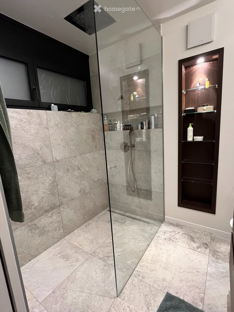 Modern bathroom with a glass-enclosed shower, marble tiles, a built-in cabinet, and a towel on the side.