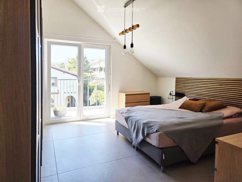 Modern bedroom with a large bed, wooden headboard, nightstand, and a view of a balcony through large glass doors.