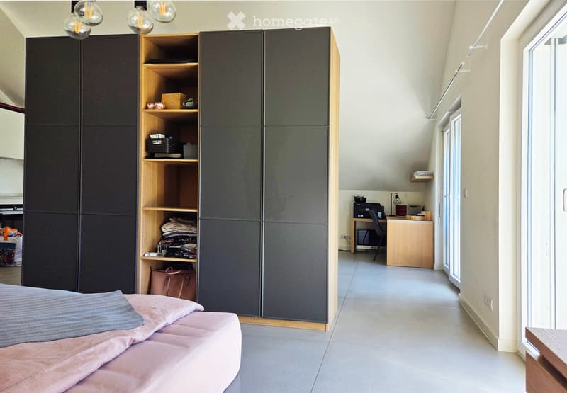 Modern bedroom with a bed, large wardrobe, shelves, desk, and chair. The room features light-colored walls and a tiled floor.