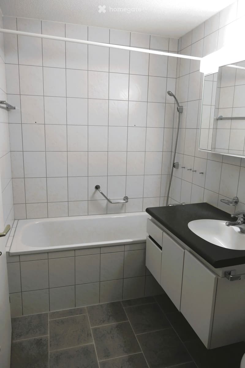 Bathroom with white tiles, bathtub, sink, mirror, shower head, and cabinet