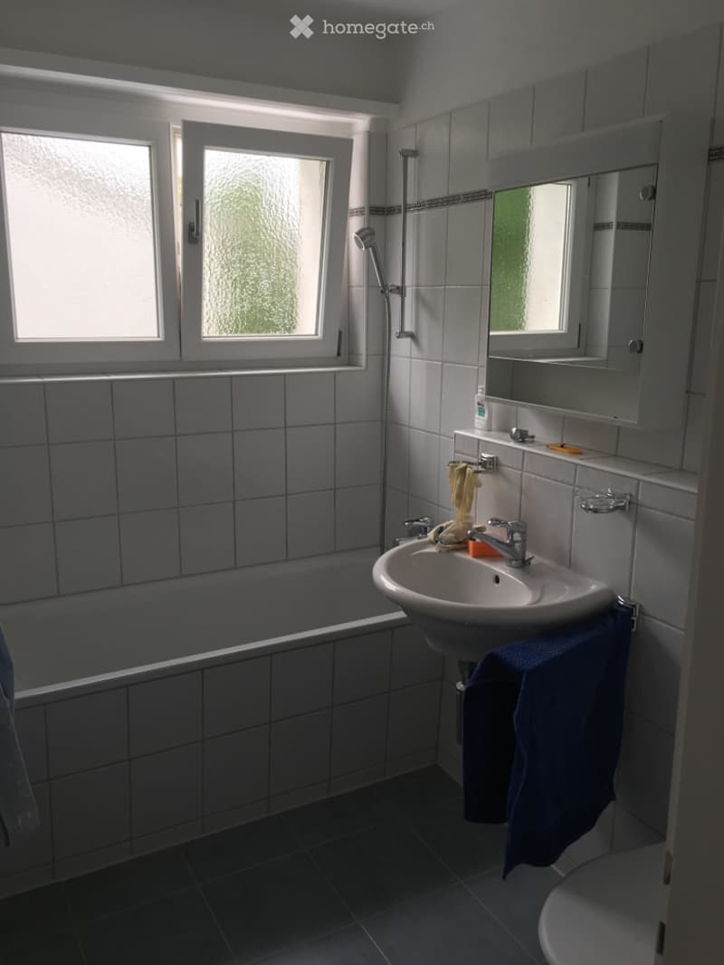 Bathroom with tiled walls and floor, a bathtub, a sink with a mirror above it, and a shower in the corner.