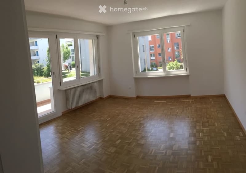 Empty room with wooden flooring, large windows, and radiator. No furniture or equipment present.