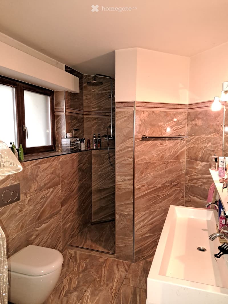 Modern bathroom with marble tiles, a bathtub, toilet, shower, and various toiletries on the counter.