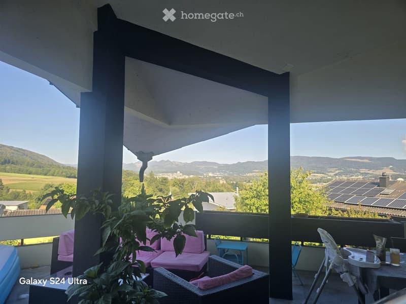 Balcony with a view of the countryside, featuring a pink sofa, wicker chairs, a small table, and a baby chair.