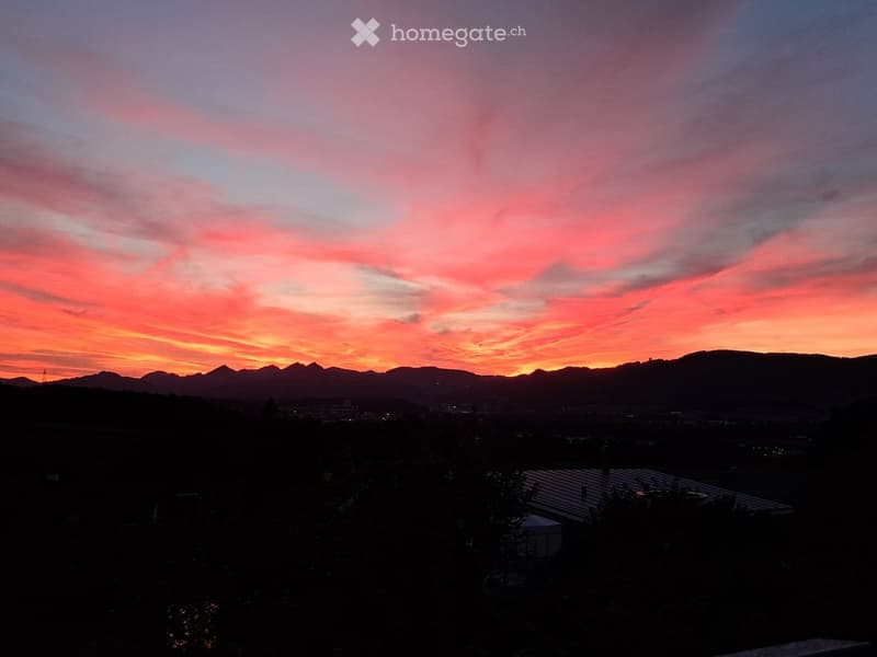 A scenic view of a sunset over a cityscape with mountains in the background, featuring vibrant pink and orange hues in the sky.