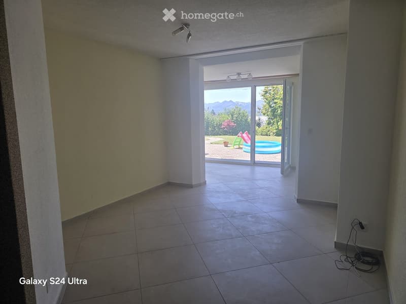 Empty room with tiled floor, white walls, and large sliding glass doors leading to a patio with a swimming pool visible outside.