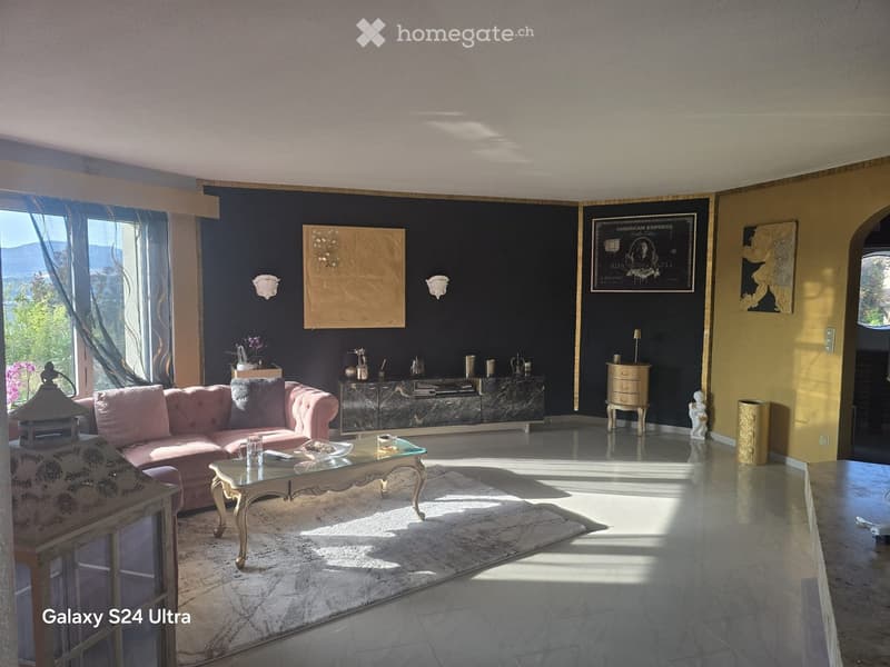 Elegant living room with a pink tufted sofa, glass coffee table, decorative cabinet, and large windows offering a scenic view.