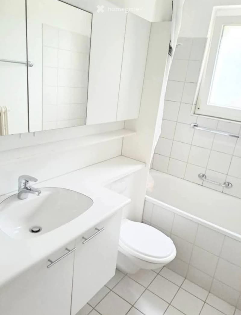 Modern bathroom with white tiles, a sink with a chrome faucet, a toilet, a bathtub, and a mirrored cabinet.
