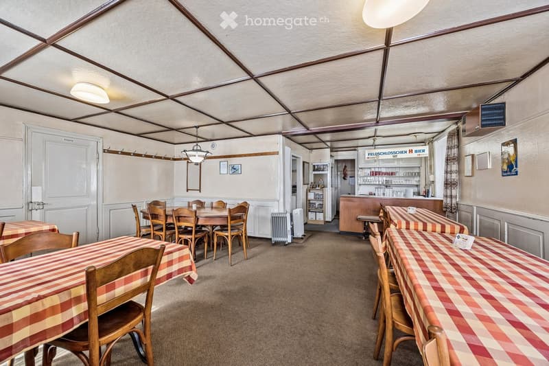 Restaurant or dining area with wooden tables and chairs, checkered tablecloths, a bar area with shelves, and a mirror on the wall.