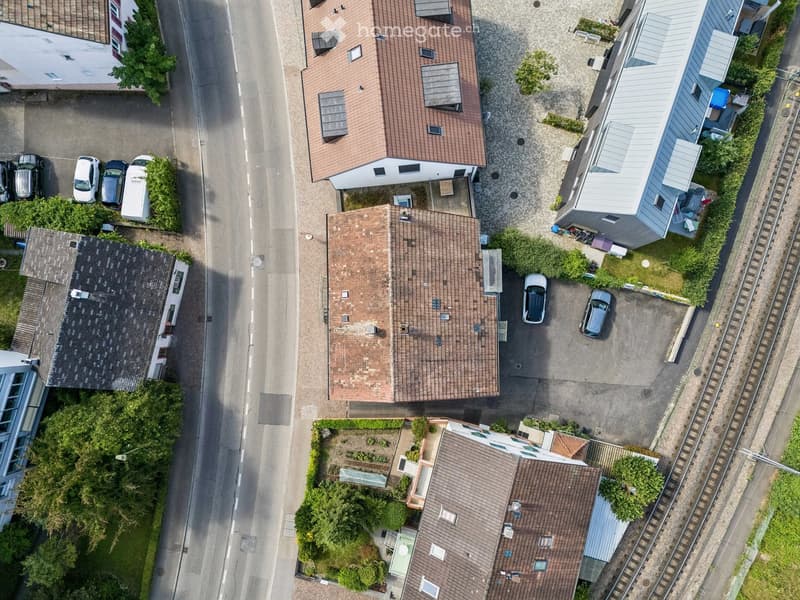 Aerial view of a residential area with multiple houses, parked cars, and surrounding greenery.