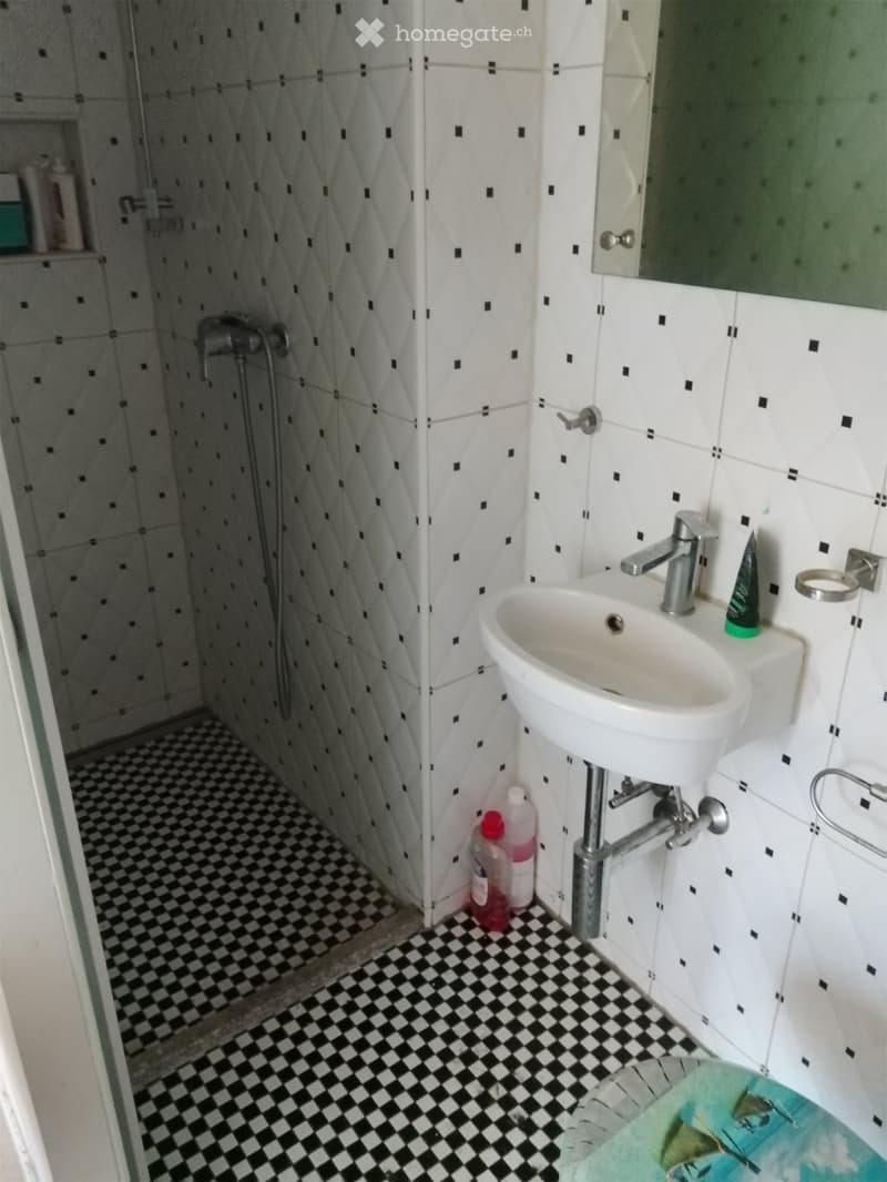 Bathroom with white tiles, black and white checkered floor, sink, mirror, and shower area.