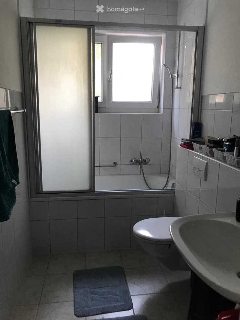 Bathroom with tiled walls and floor, featuring a toilet, sink, bathtub, shower stall, towel, bathmat, and cabinet.