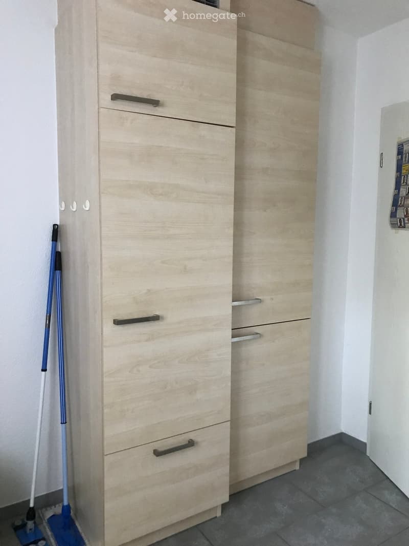 Empty room with light wooden cabinets and a broom leaning against the wall.