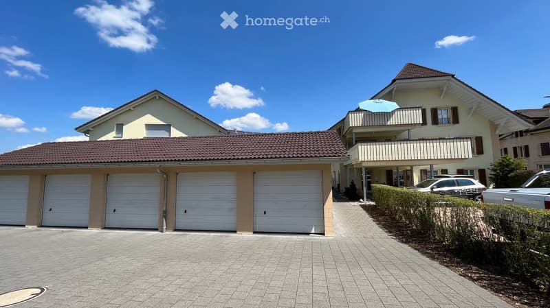 Two-story house with a tiled roof, multiple garage doors, and a balcony with an umbrella on the upper level.