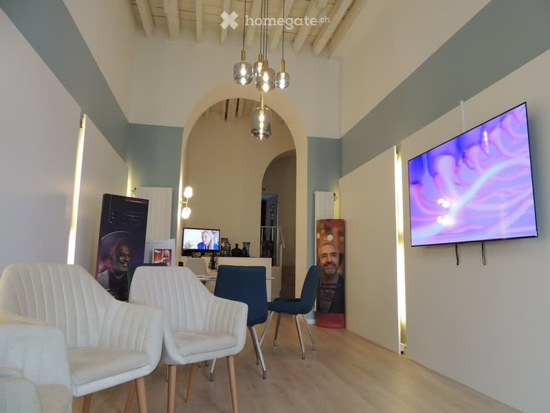 Modern waiting area with white and blue chairs, a small table, and two screens mounted on the walls.