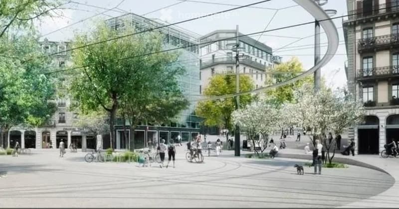 A modern urban square with trees, benches, and people walking. The area features a curved pathway, modern buildings in the background, and a mix of pedestrians and cyclists.