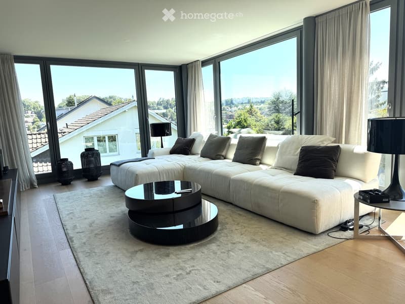 Modern living room with large windows offering a scenic view, featuring a white sectional sofa, a black coffee table, floor lamps, side tables, and decorative vases.