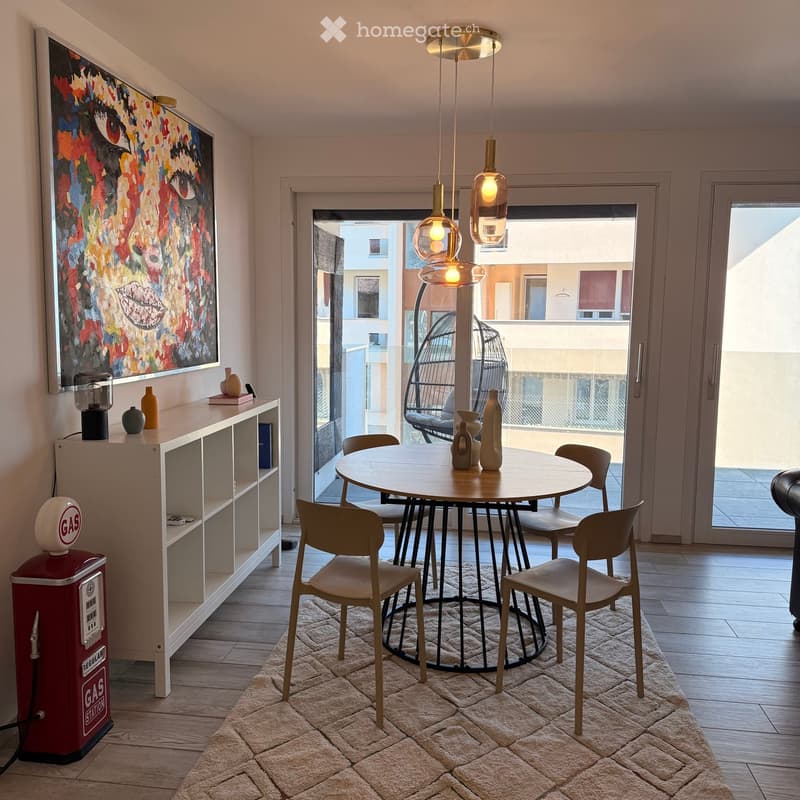 Modern living room with a round wooden table, six chairs, a shelf with decorative items, a colorful painting, and a view to a balcony with a wicker hanging chair.