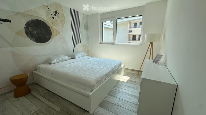 Modern bedroom with a white bed, nightstand, floor lamp, and a decorative stool near the bed.