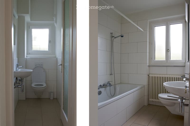 Two adjacent bathrooms with white tiled walls and floors, each equipped with a sink, toilet, and bathtub. The left bathroom features a window above the sink, while the right bathroom includes a showerhead and a radiator.