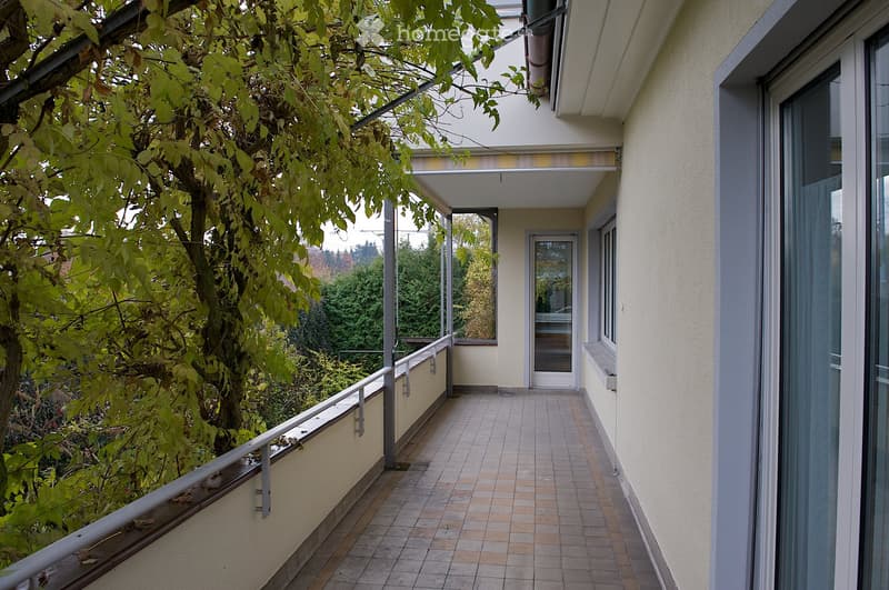 Balcony with tiled floor, metal railing, and a view of greenery and trees.