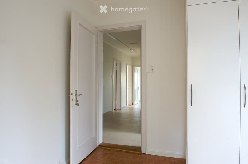 Empty hallway with wooden flooring, white walls, and multiple doors leading to other rooms.