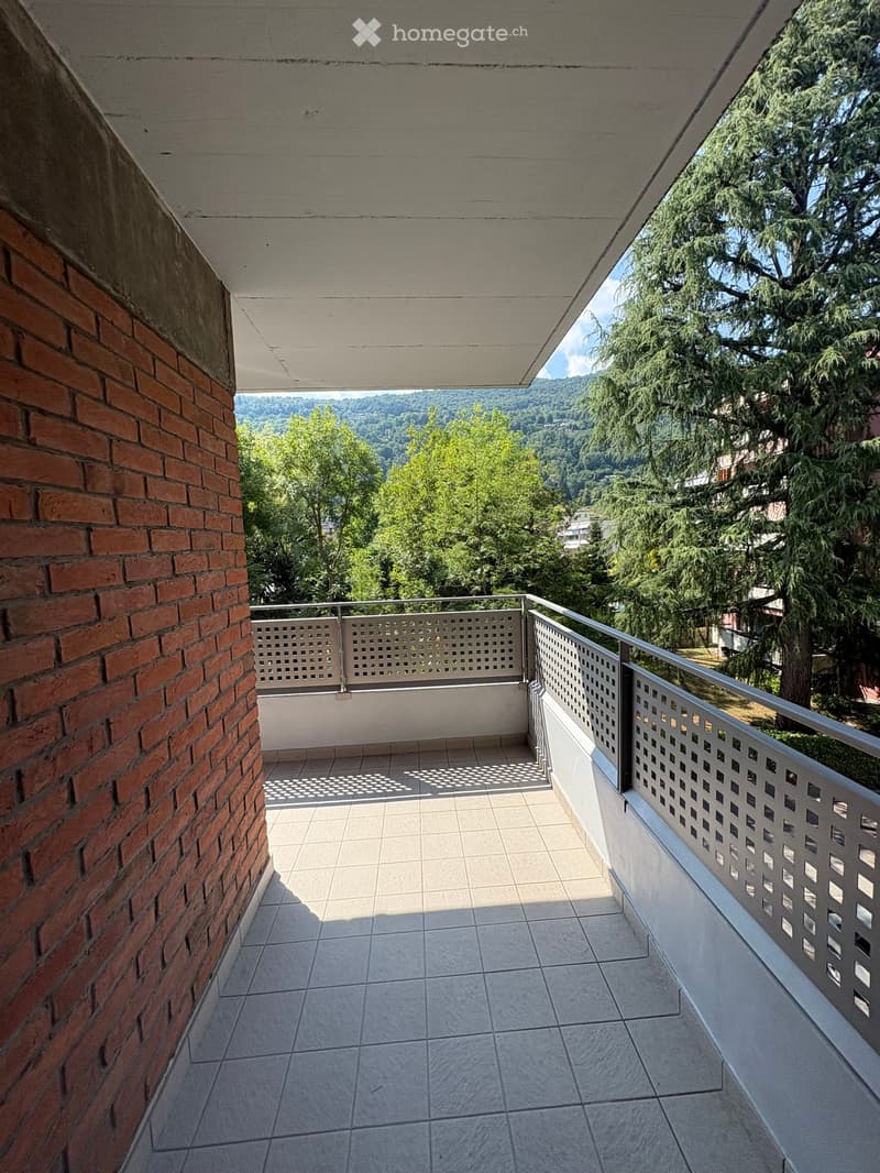 Balcony with tiled floor, metal railing, and scenic view of trees and hills.