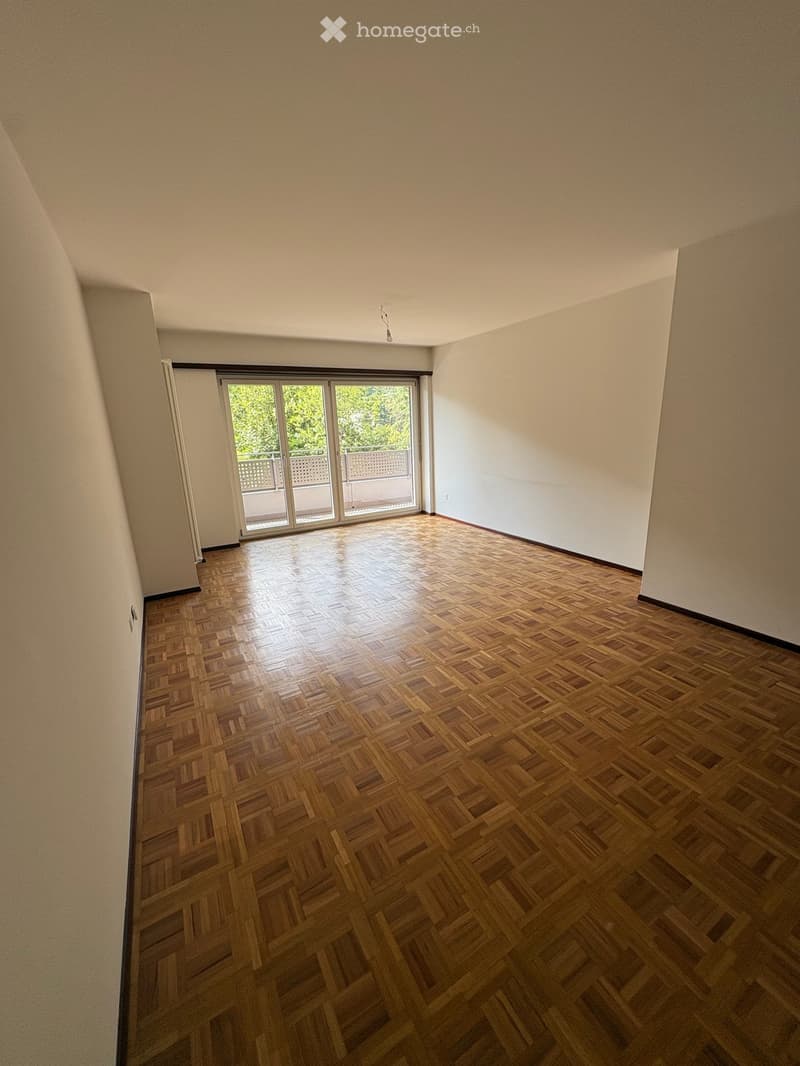 Empty room with wooden parquet flooring, white walls, and a large sliding glass door leading to a balcony.