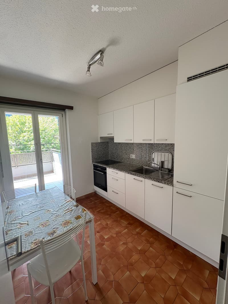 Modern kitchen with white cabinets, granite countertop, and a dining area with a table and chairs. Features a sliding glass door leading to a balcony.