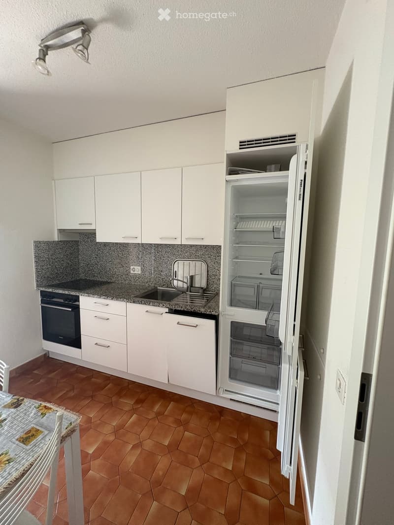Modern kitchen with white cabinets, granite countertop, stainless steel sink, and open refrigerator. Features include an oven, faucet, and tiled floor.
