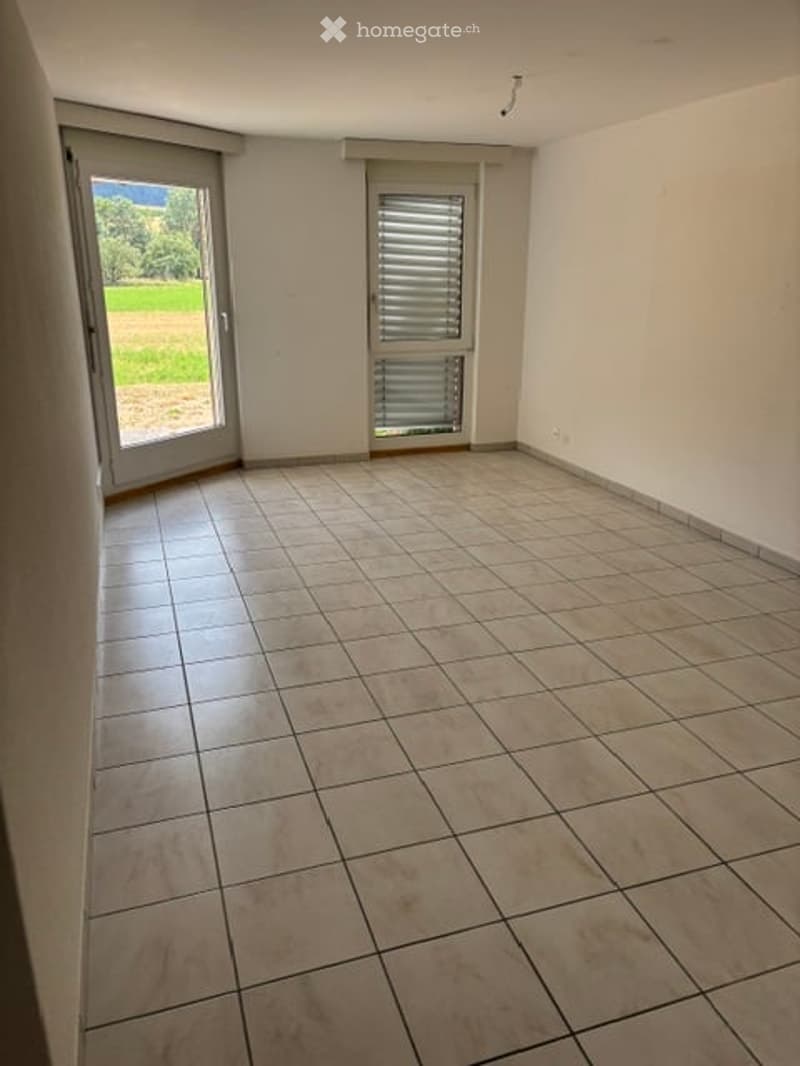 Empty room with tiled floor, white walls, large sliding glass door leading to outdoor area, and a smaller window with blinds.