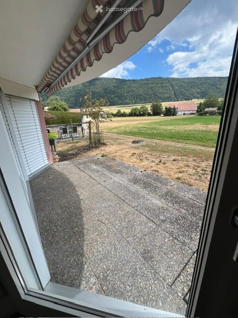 Balcony with striped awning overlooking a grassy field and distant hills.
