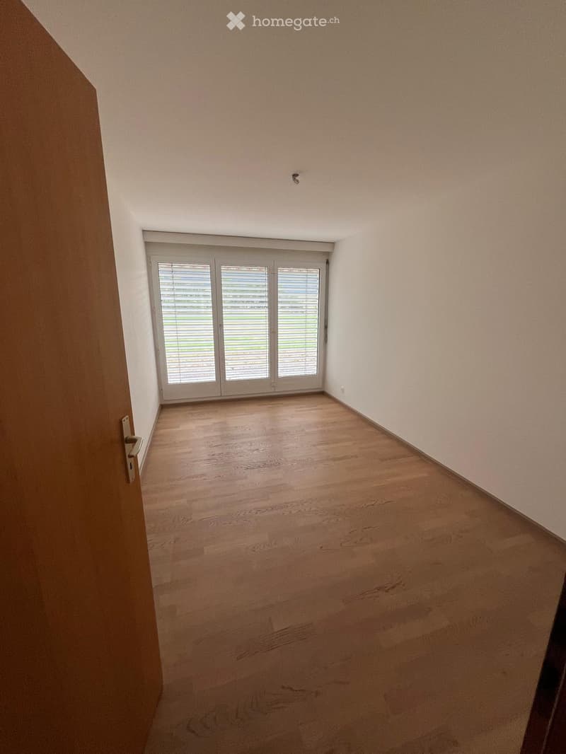 Empty room with wooden flooring, white walls, and a large sliding glass door with blinds.