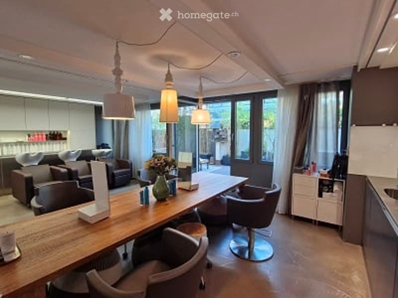Modern, open-plan living and dining area with a large wooden table, chairs, sofas, and a kitchen area with cabinets and a sink.