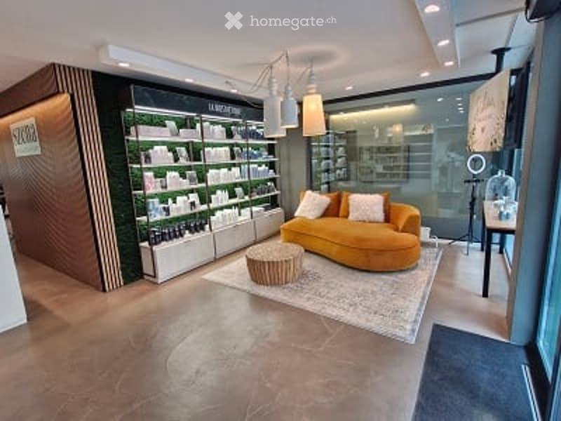 Modern, well-lit room with a curved orange sofa, a round coffee table, a large area rug, and shelves filled with various items. The space features contemporary decor with warm lighting and a sleek design.