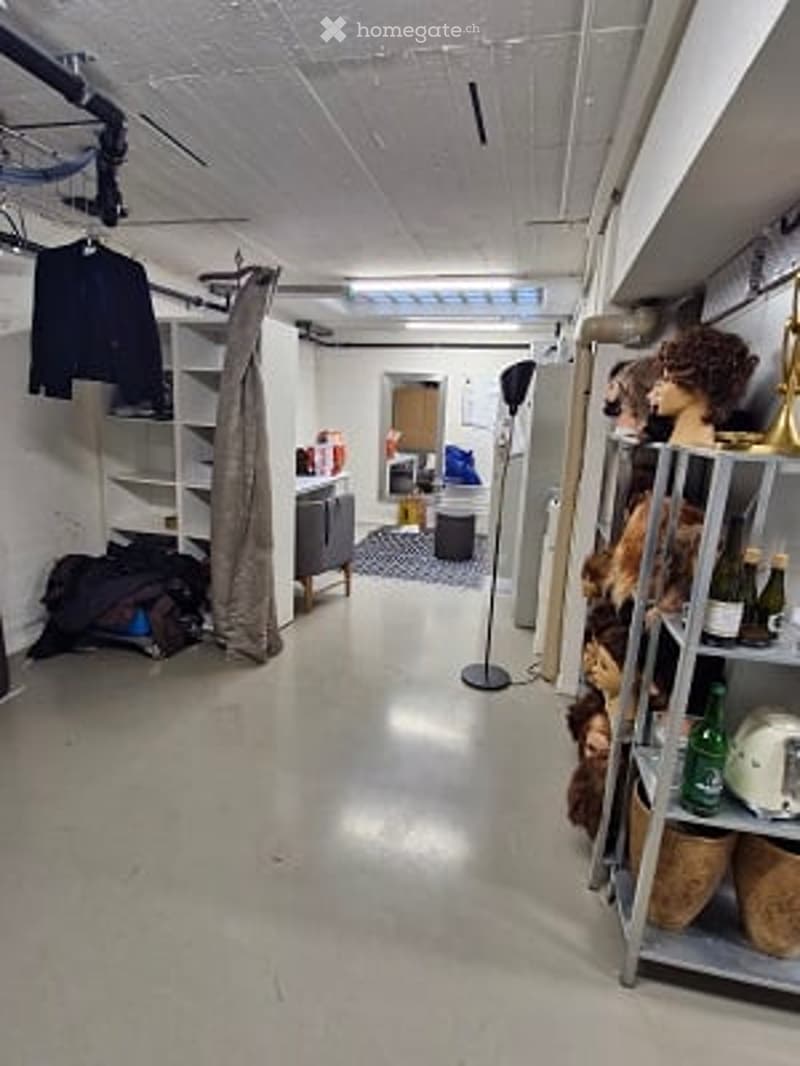 Empty room with white walls, exposed ceiling pipes, and storage shelves. No furniture or equipment present.