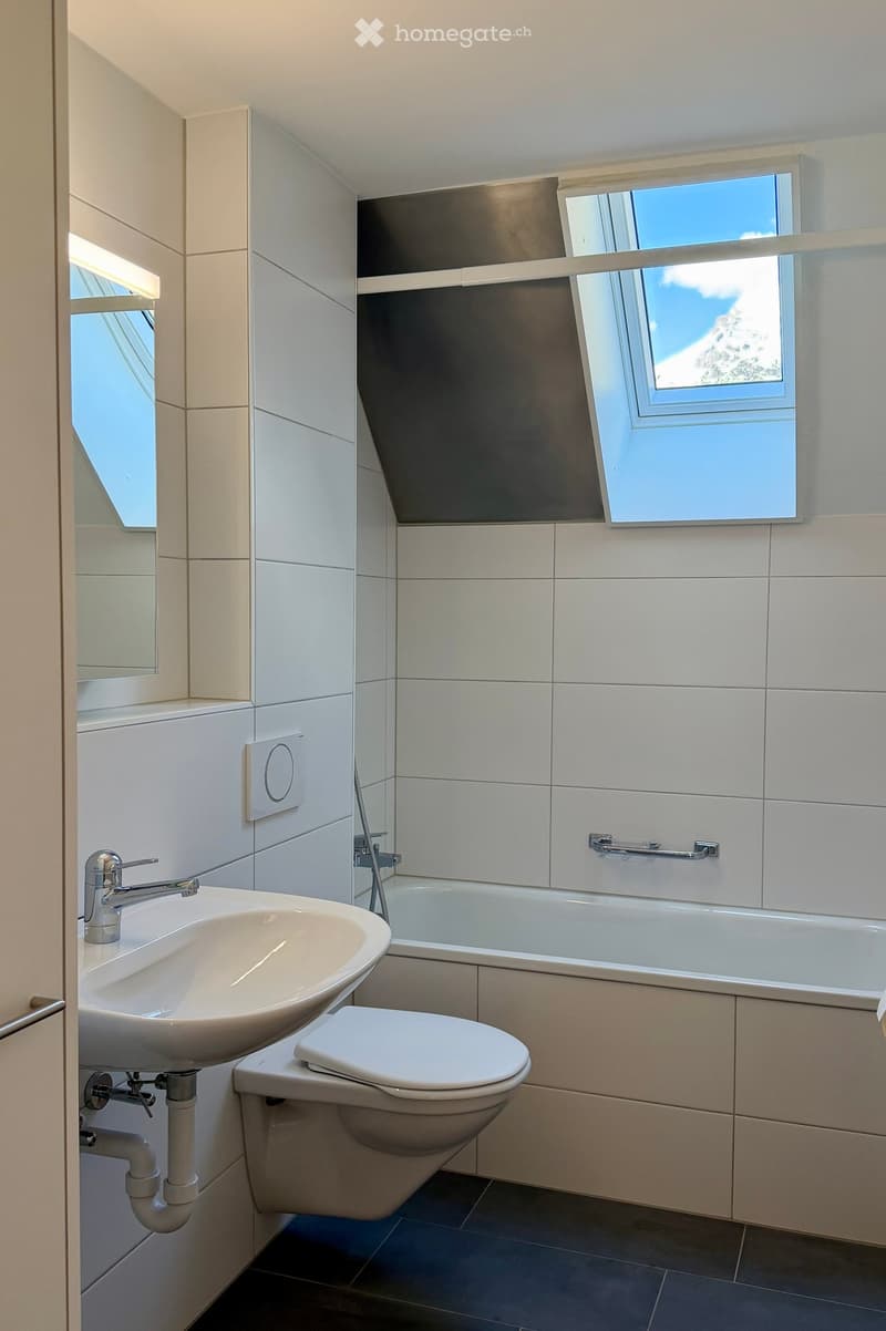 Modern bathroom with white tiles, a sink with a modern faucet, a toilet, a bathtub, and a large window offering a scenic view.