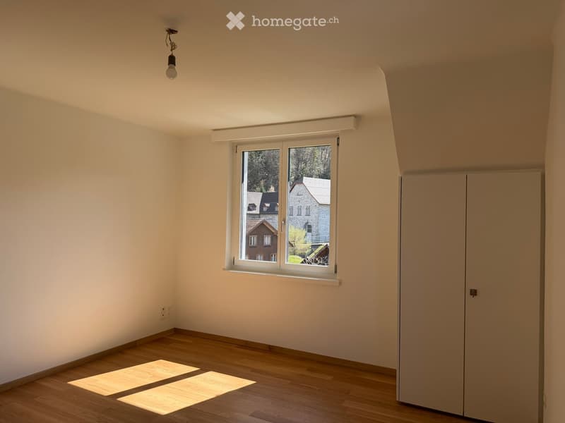 Empty room with wooden flooring, white walls, a large window with white frame, and a built-in closet. Natural light streams in from the window.